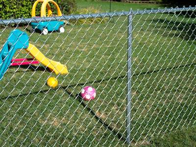 Aluminum coated chain link mesh with round posts for residential use outdoor play area protection.